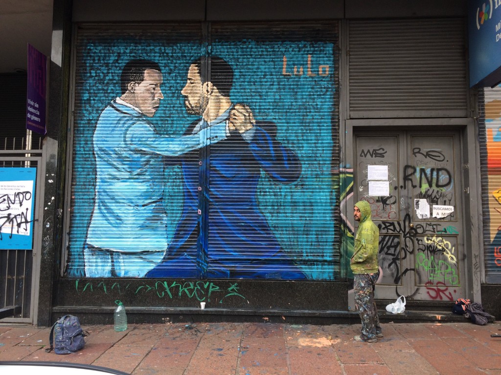 Artist Lulo standing beside his tango mural of two dancers painted on a shop shutter